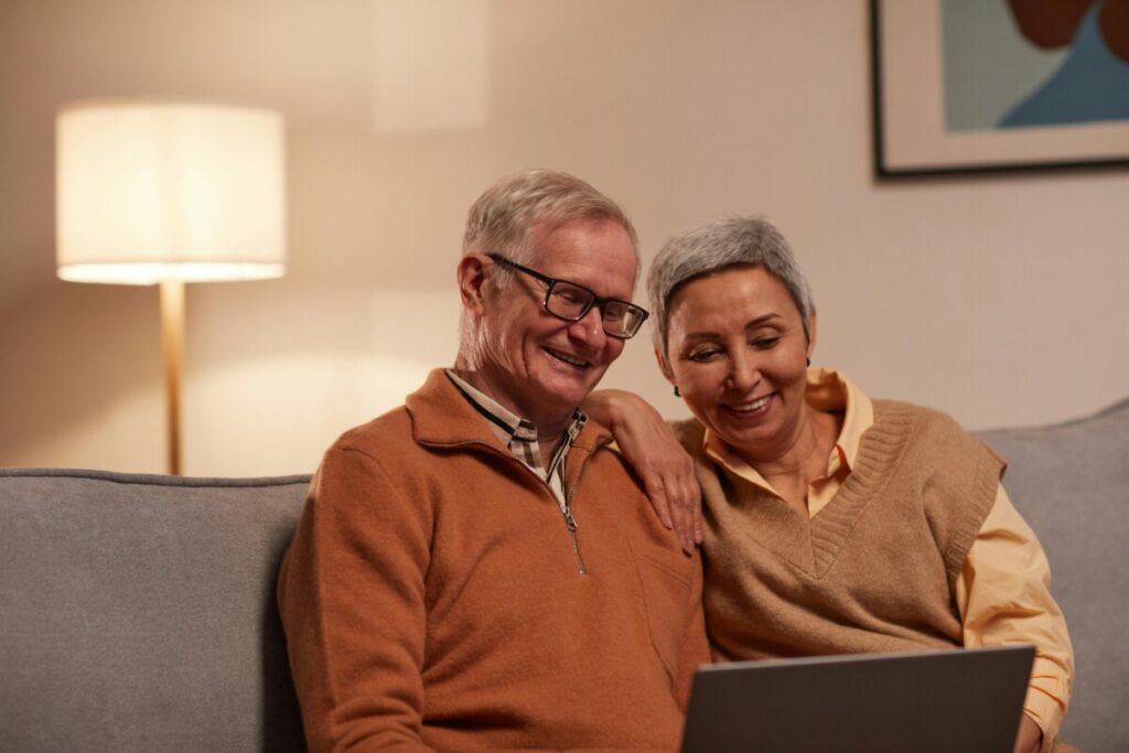 two elderly people sitting on a couch looking at a laptop